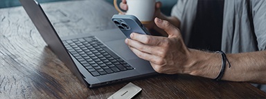 Un homme utilisant son iPhone 5 Pro avec un SSD Kingston XS2000 et un portable MacBook pro sur la table