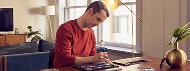 Un homme chez lui, assis à une table, installant un SSD dans son ordinateur portable ouvert avec des outils à proximité