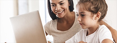 eine Mutter und Tochter lächelnd zu Hause am Tisch sitzend mit einem Laptop