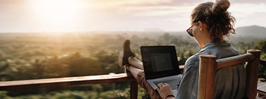 Une jeune femme travaillant sur un ordinateur portable au coucher du soleil sur un balcon