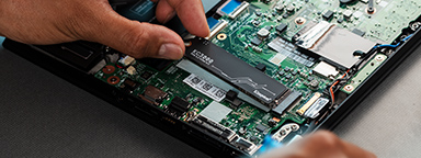 Deux mains travaillent sur une carte mère posée sur un bureau, pour installer un SSD M.2.